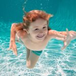 Junge Schwimmt unter Wasser mit offenen Augen und freut sich