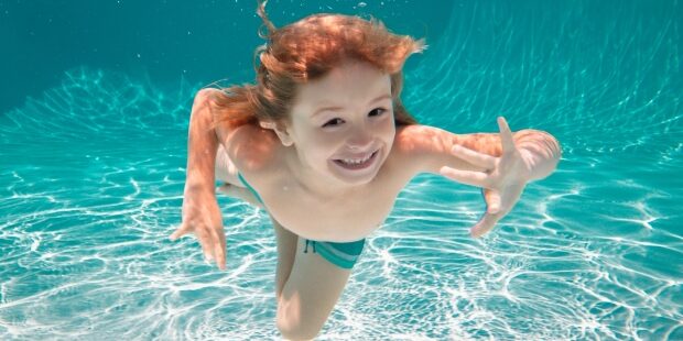 Junge Schwimmt unter Wasser mit offenen Augen und freut sich