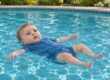 Baby im blauen Schwimmanzug schwebt allein auf dem Rücken an der Wasseroberfläche eines Außenpools.