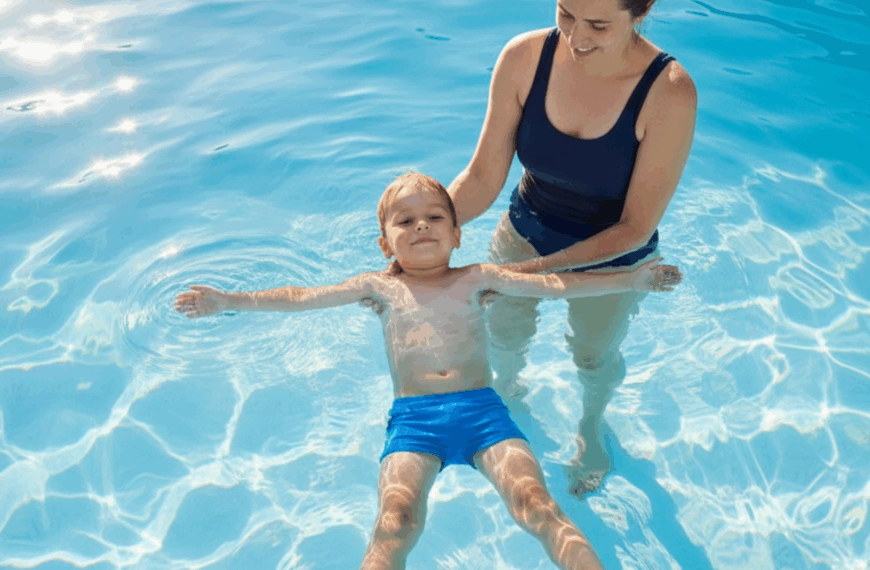 Basiskompetenzen lernen: Ein kleiner blonder Junge schwebt auf dem Rücken im Wasser, mit ausgebreiteten Armen und Beinen. Seine Mutter hält stützend die Hände unter seinem Körper.